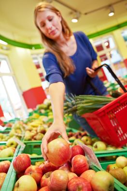 Frau greift im Supermarkt nach einem Apfel aus dem Obstregal