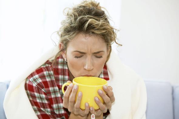 Eine Frau hat eine Grippe und trinkt einen heiße Tasse Tee.
