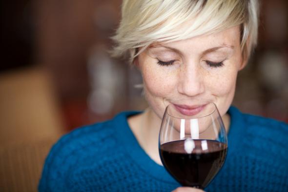 Junge Frau riecht am Rotweinglas um den Duft des Weines aufzunehmen.