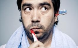 Mann putzt sich die Zähne, während aus dem linken Ohr die Zahnbürste herausschaut