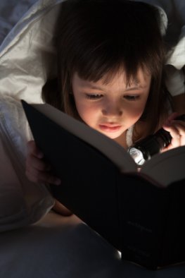 Lesen in der Dämmerung - Mädchen liest mit Taschenlampe ein Buch im Bett