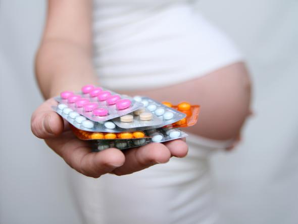 Schwangere Frau hält einige Tabletten-Blister in der Hand.