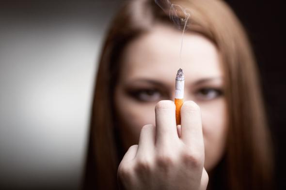 Junge Frau blickt auf eine Hand in der eine Zigarette qualmt.