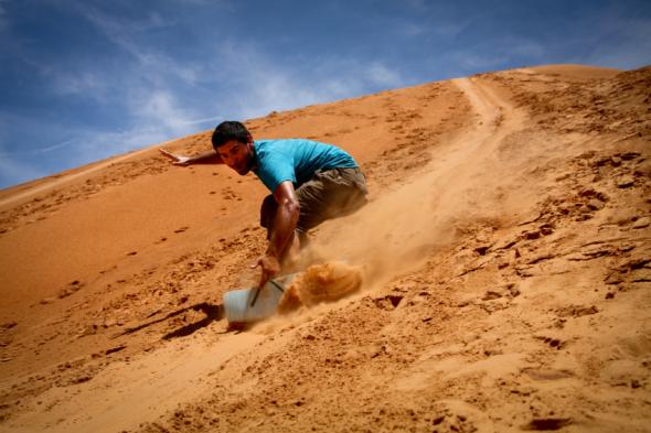 Junger Mann gleitet mit einem Board die Sanddünen hinunter.