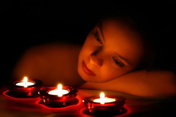 Junge Frau schaut depremiert in das Kerzenlicht.